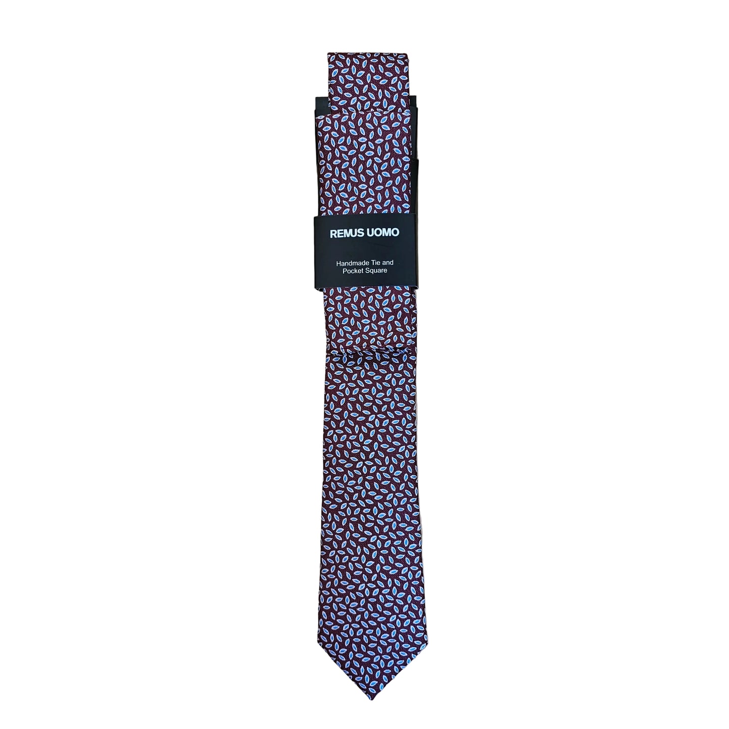 A patterned necktie with a small geometric print in purple, pink, and white, folded with a black paper band that reads 'REMAE LOMBO' on a light wood background.