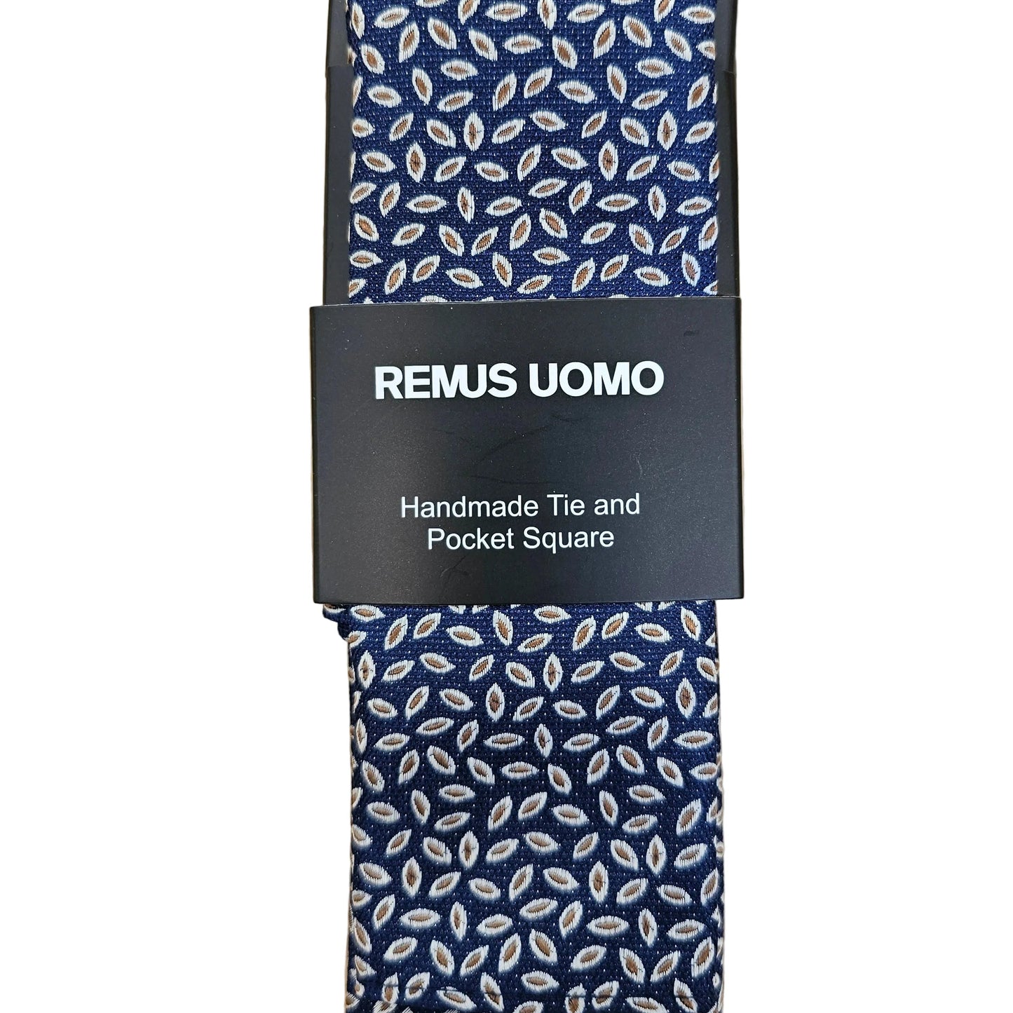 A navy blue necktie with a white leaf pattern, wrapped in a black paper band labeled 'REMUS UOMO Handmade Tie and Pocket Square', laid flat on a light wood background.