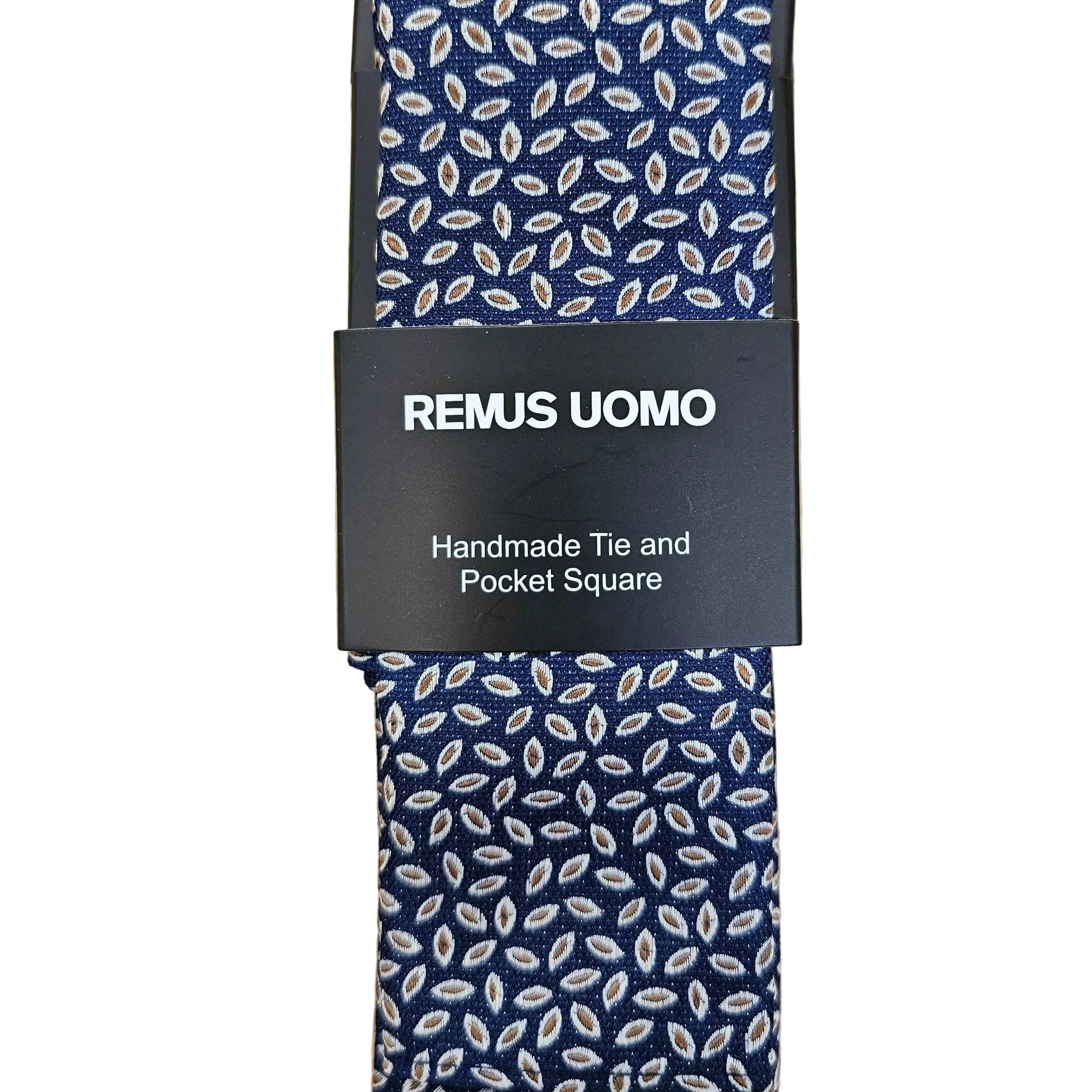 A navy blue necktie with a white leaf pattern, wrapped in a black paper band labeled 'REMUS UOMO Handmade Tie and Pocket Square', laid flat on a light wood background.