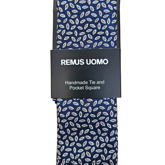 A navy blue necktie with a white leaf pattern, wrapped in a black paper band labeled 'REMUS UOMO Handmade Tie and Pocket Square', laid flat on a light wood background.