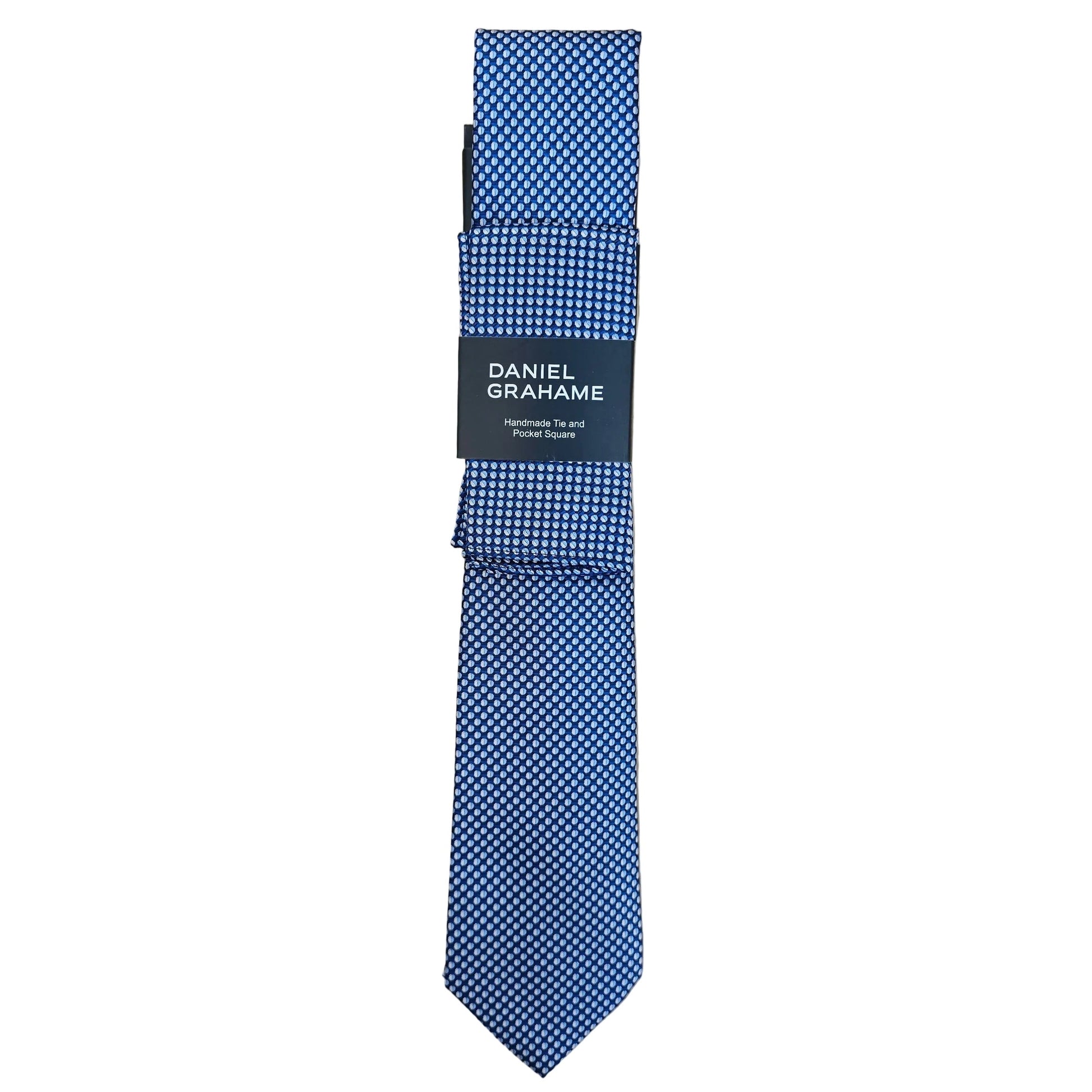 A folded blue and white patterned necktie with a black paper band label reading 'DANIEL GRAHAME', placed on a light wood grain surface.
