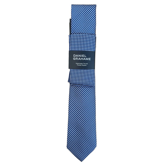 A folded blue and white patterned necktie with a black paper band label reading 'DANIEL GRAHAME', placed on a light wood grain surface.