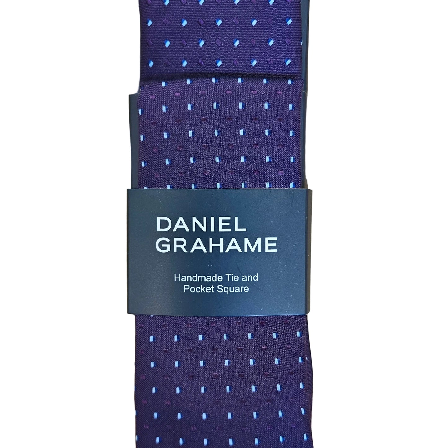 A folded Daniel Grahame necktie in a deep purple hue with a small light blue dotted pattern, wrapped in a black paper band displaying the brand name, laid flat on a light wood grain surface.