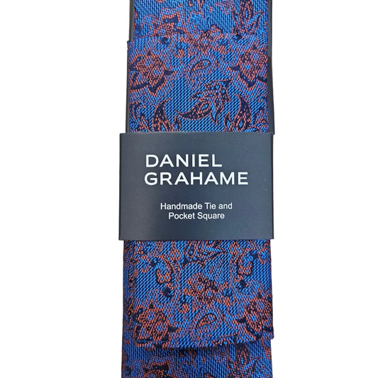 A Daniel Grahame patterned tie laid flat on a light wood surface, wrapped with a black paper band showing the brand name in white text.