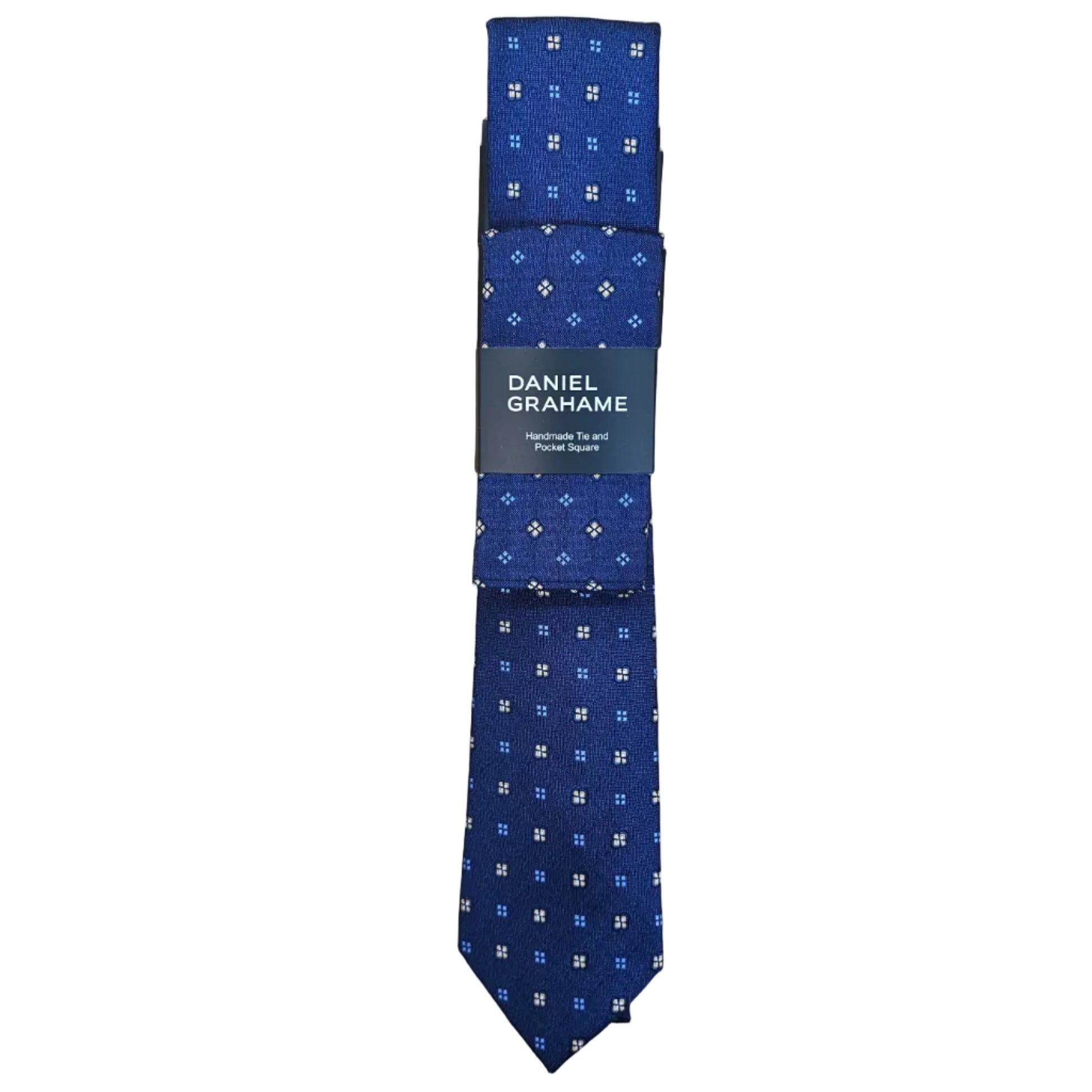 A folded blue necktie with a small white and light blue geometric pattern, wrapped in a black paper band labeled 'DANIEL GRAHAME', placed on a light wood grain surface.