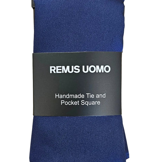 A navy blue square tie wrapped in a black paper band labeled 'REMUS UOMO', placed on a light wood grain surface.