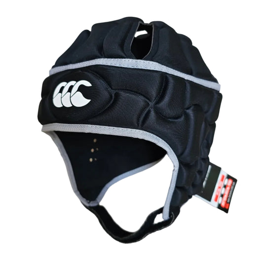 Black padded protective headgear with gray trim and a white logo, photographed on a light wood floor with a retail tag attached.