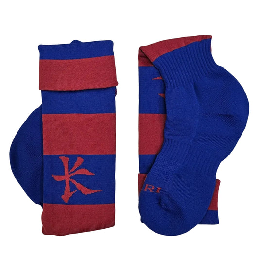 A pair of blue and maroon striped athletic socks laid flat on a light wood floor. One sock is folded to show a blue heel with a maroon Kukri logo, and the other is laid flat showing the blue ribbed cuff and maroon toe.